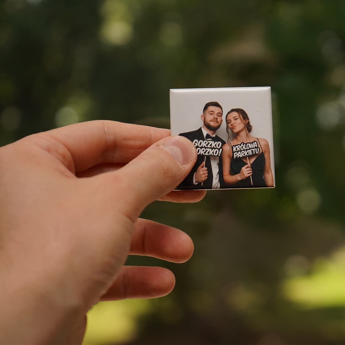 Dłoń trzymająca foto-magnes pary młodej na tle zieleni